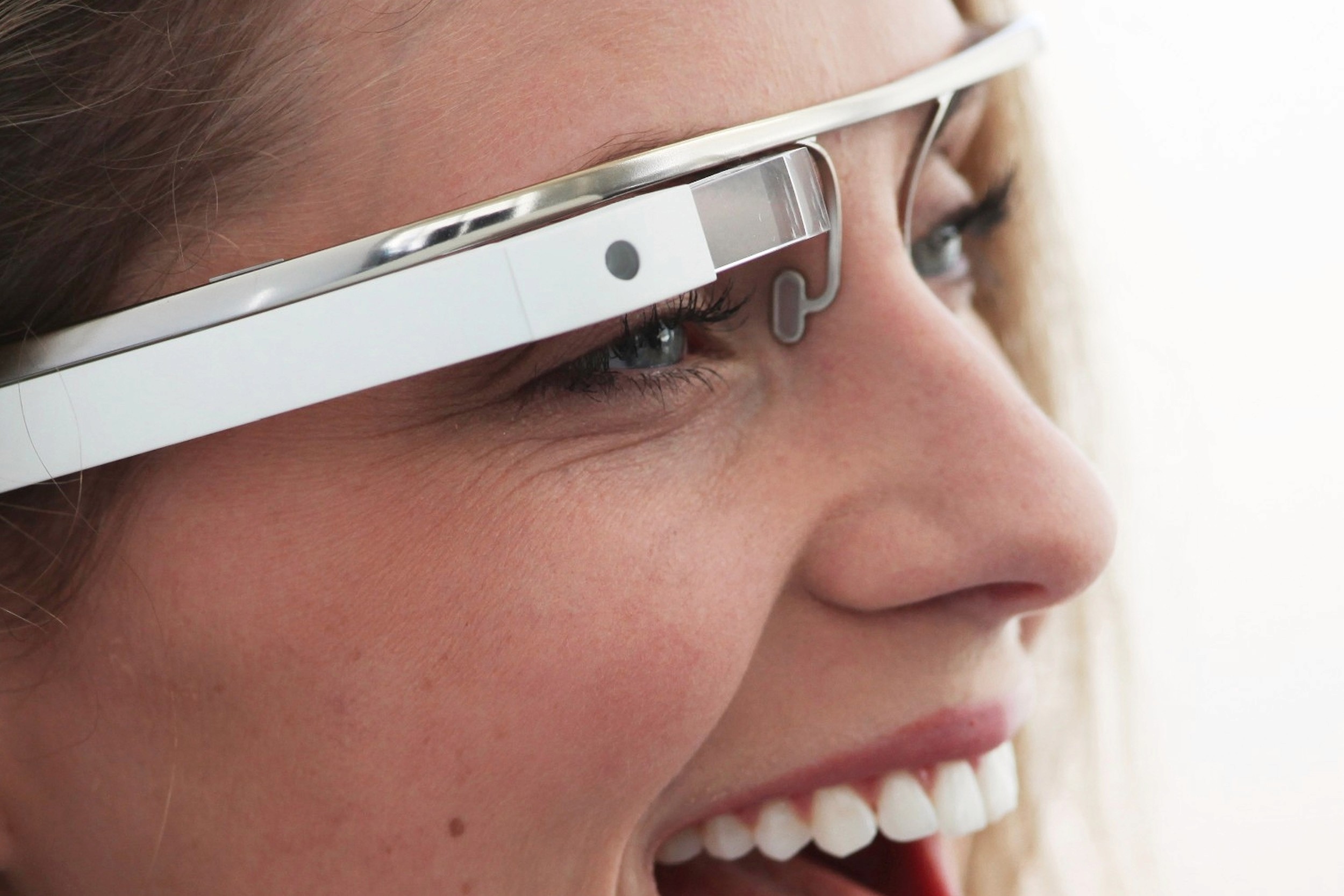 A close-up of a woman smiling and wearing white Google Glass.