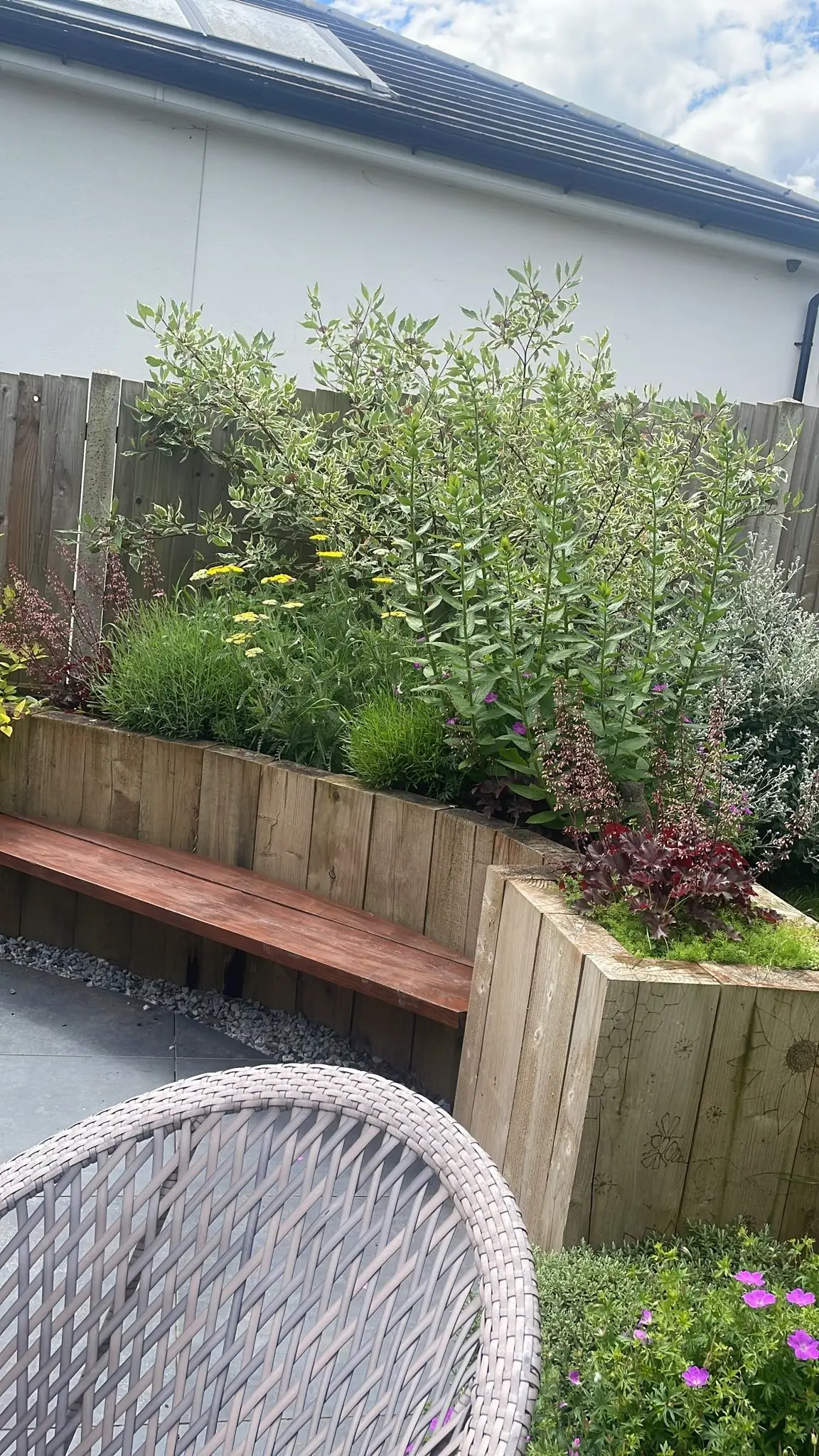 A cozy garden scene featuring a wooden bench and lush greenery against a house wall.
