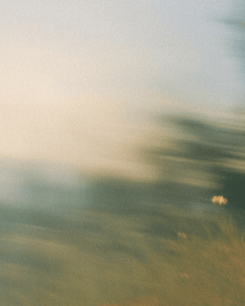 Grainy, motion-blurred abstract background with soft golden light fading into muted green and blue-gray tones.