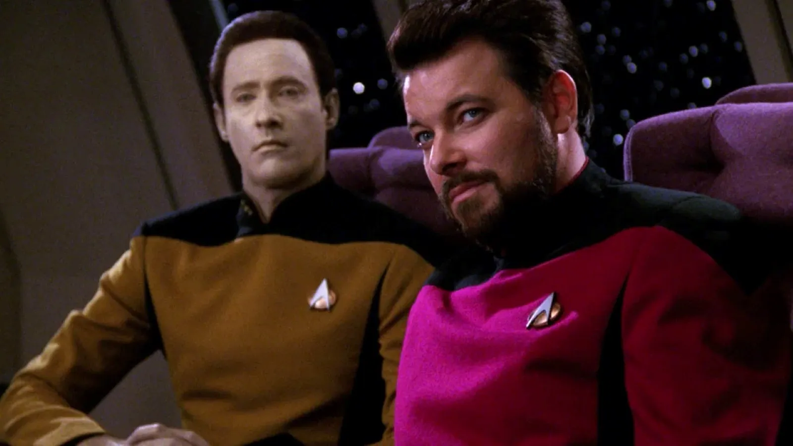 Two characters in Starfleet uniforms, one in gold and the other in red, sit on a spaceship bridge, showcasing a futuristic sci-fi setting.