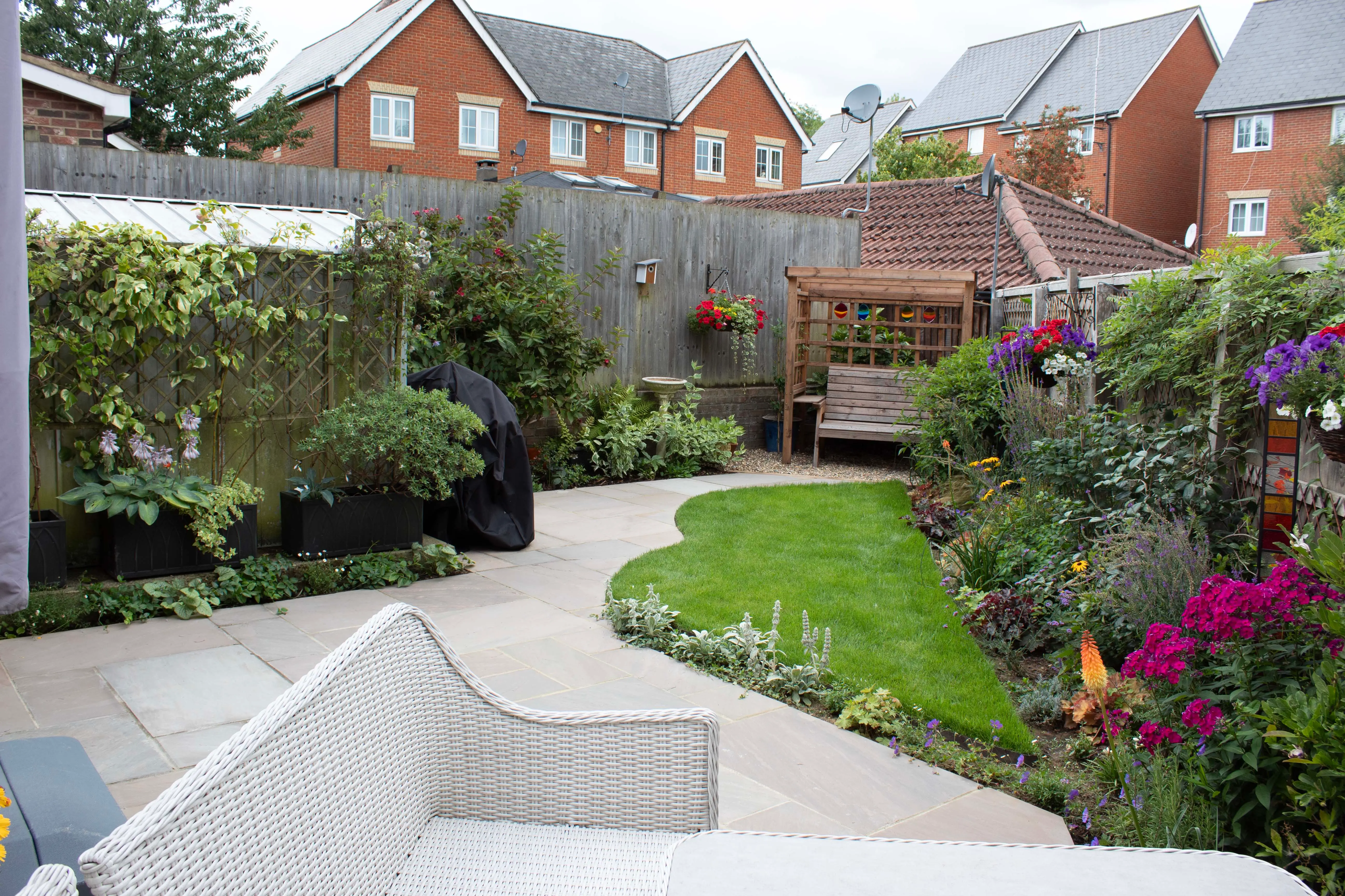 Garden pathway winding through lush greenery and colorful flowers, leading to cozy residential homes in the background.
