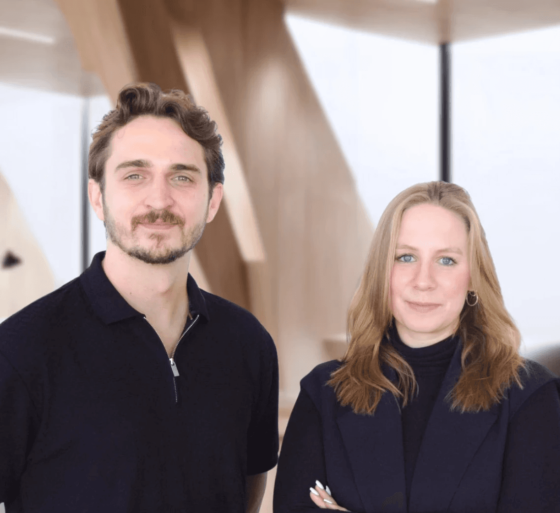 Jonas Behrend und Jamie Hartmann, Co-CEOs von Careship, Portrait eines Mannes und einer Frau stehend in einem modernen Büro mit Holzarchitektur.