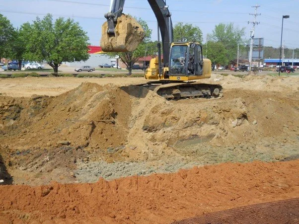 Excavator performing subgrade undercut to remove unstable soil after proof-roll failure.