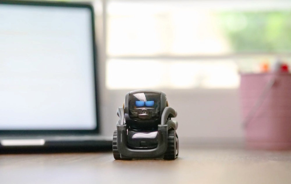 Pequeño robot sobre escritorio frente a laptop, símbolo de inversión en robótica