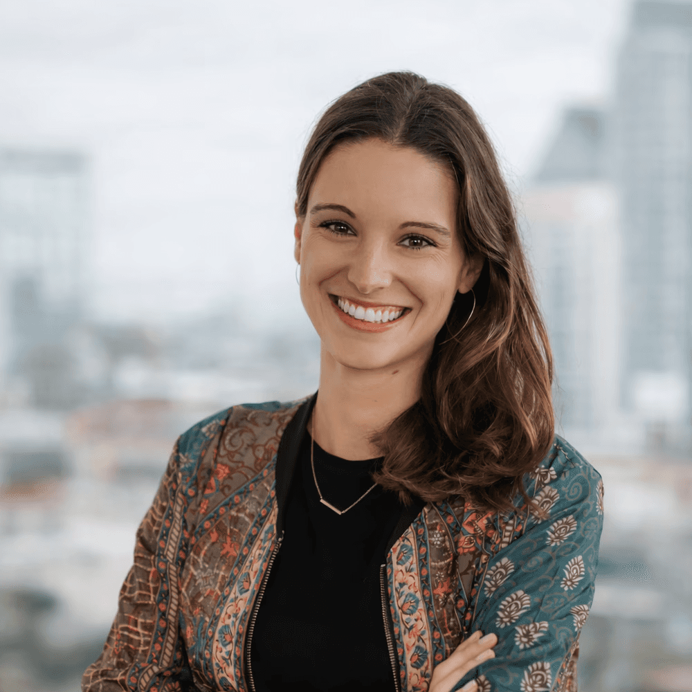 A smiling man in a suit stands in front of a blurred city background, conveying a professional appearance.