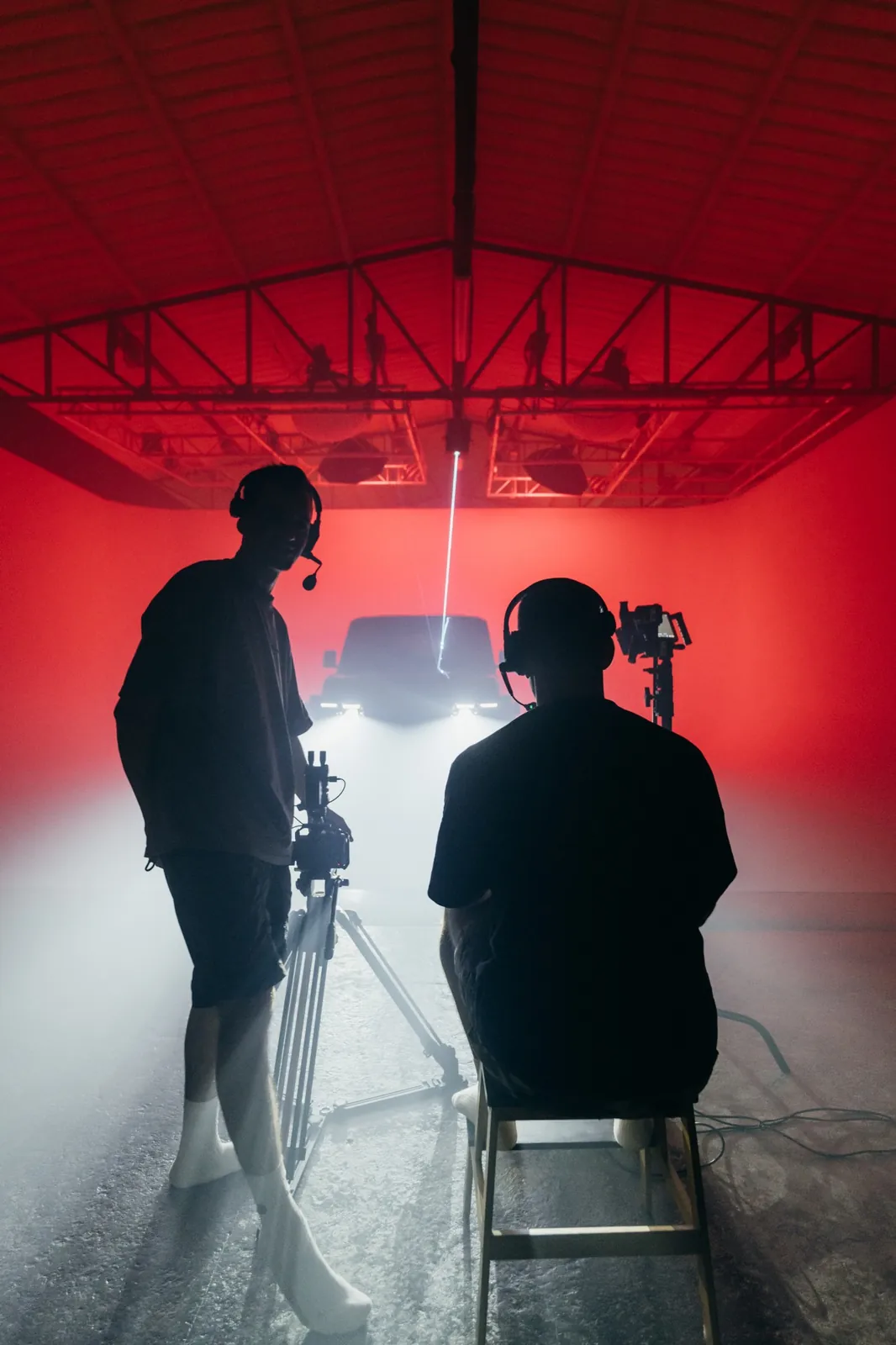 Director and camera operator in silhouette with headsets, watching the Chery V23 in red light and smoke