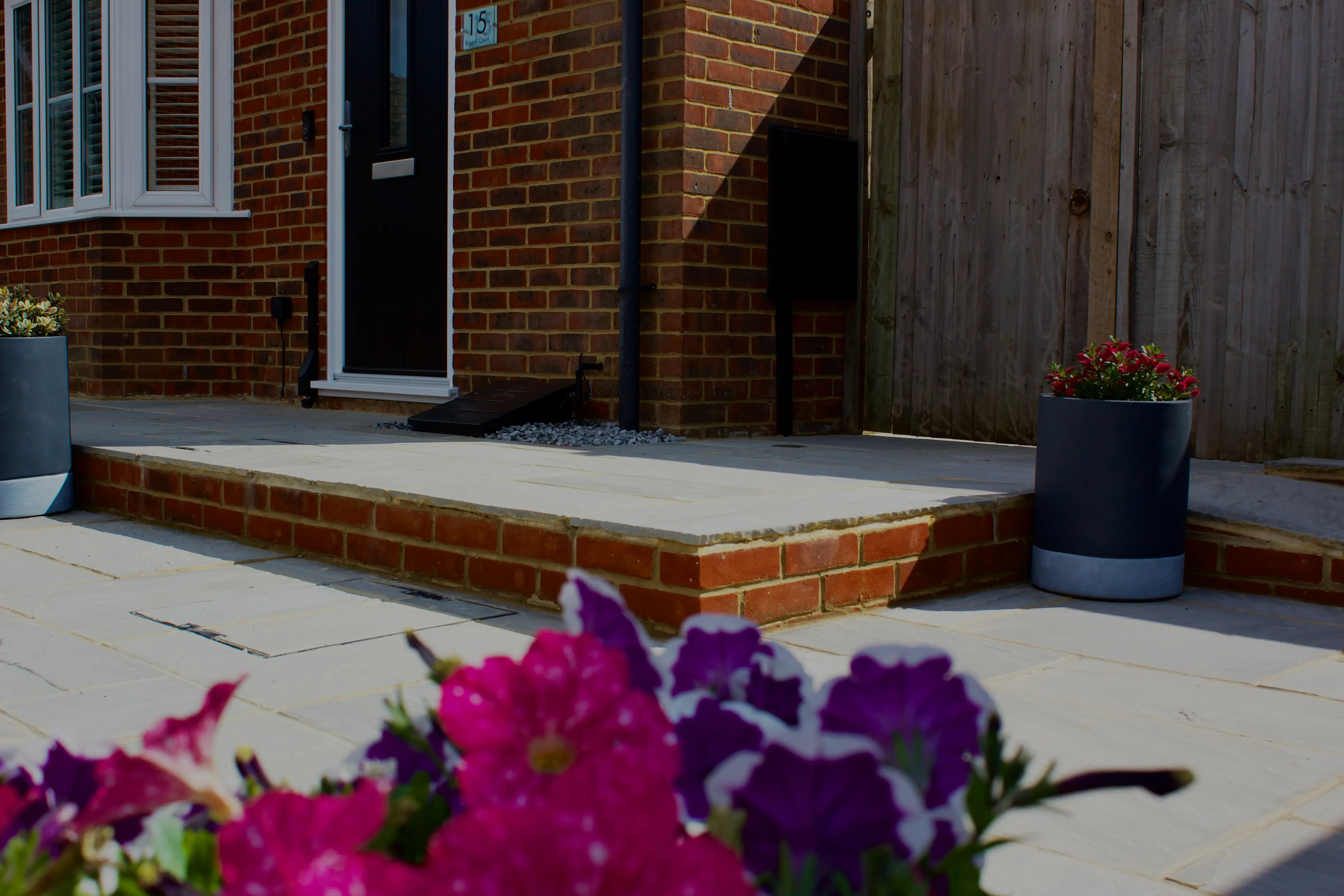 A wooden porch with steps, accompanied by vibrant purple flowers in the foreground.