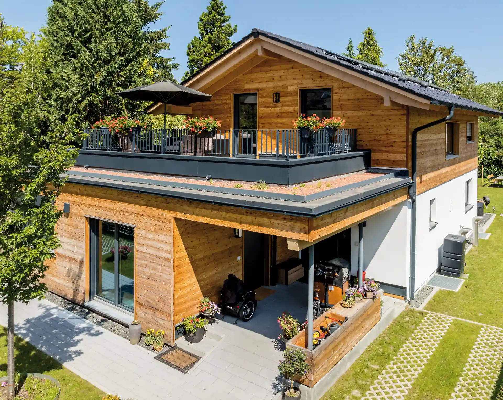 Einfamilienhaus mit Holzfassade, Dachterrasse, Carport und modernen Elementen, umgeben von Grünflächen.