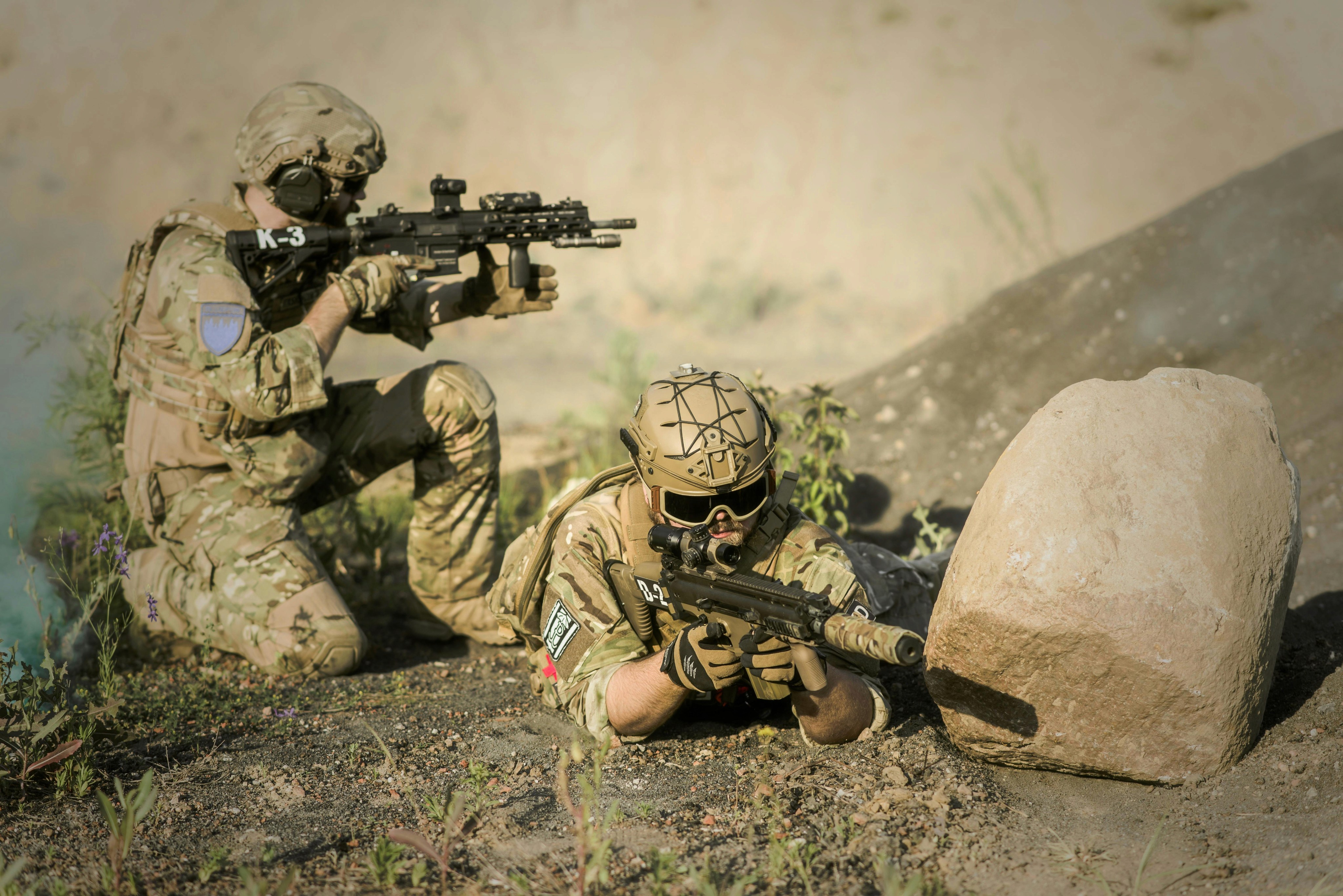 Two soldiers aiming weapons. One is lying on his stomach, while the other is kneeling on his right knee.