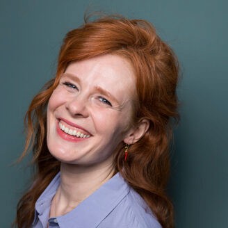 A person with curly hair standing against a blue background.
