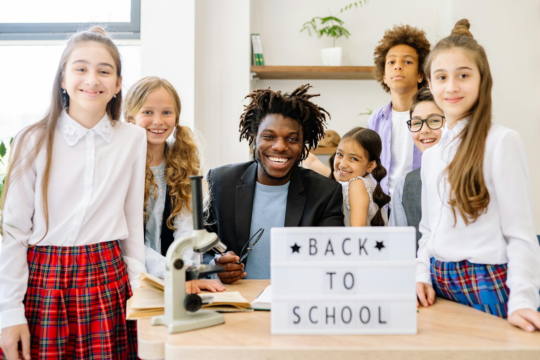 A diverse group of smiling students of various ages standing together in a bright, modern school hallway.