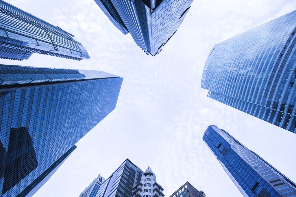 Close-up portrait of a person wearing a gray insulated hooded jacket with the hood up, showing their face framed by the hood against a light background.