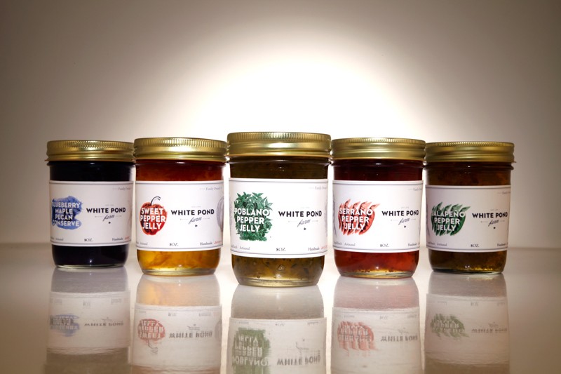 A set of glass jars with WHITE POND labels on them and green, red and blue colored plants.