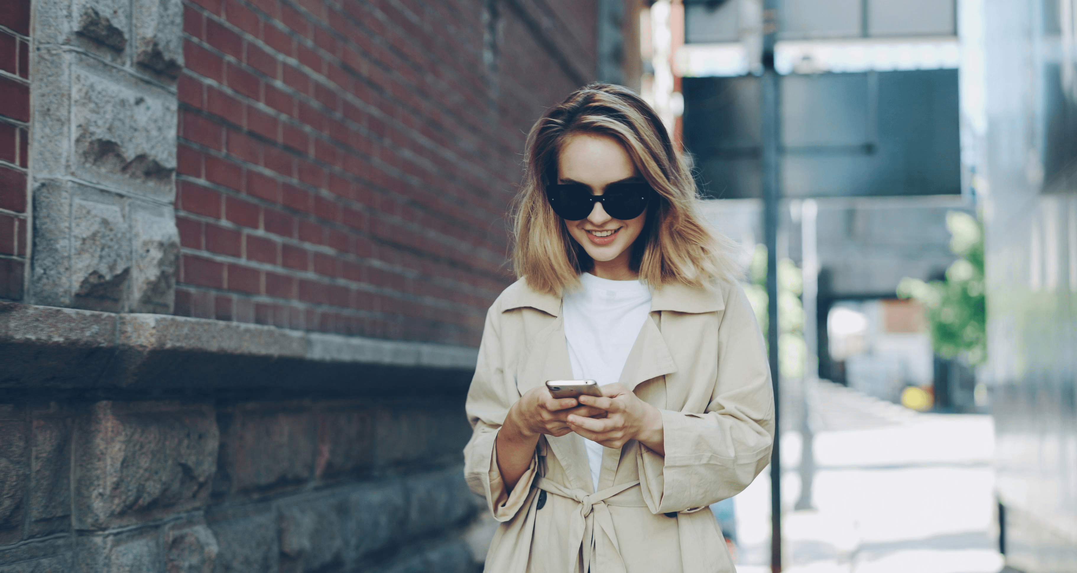 A smiling woman walks while looking at her phone.