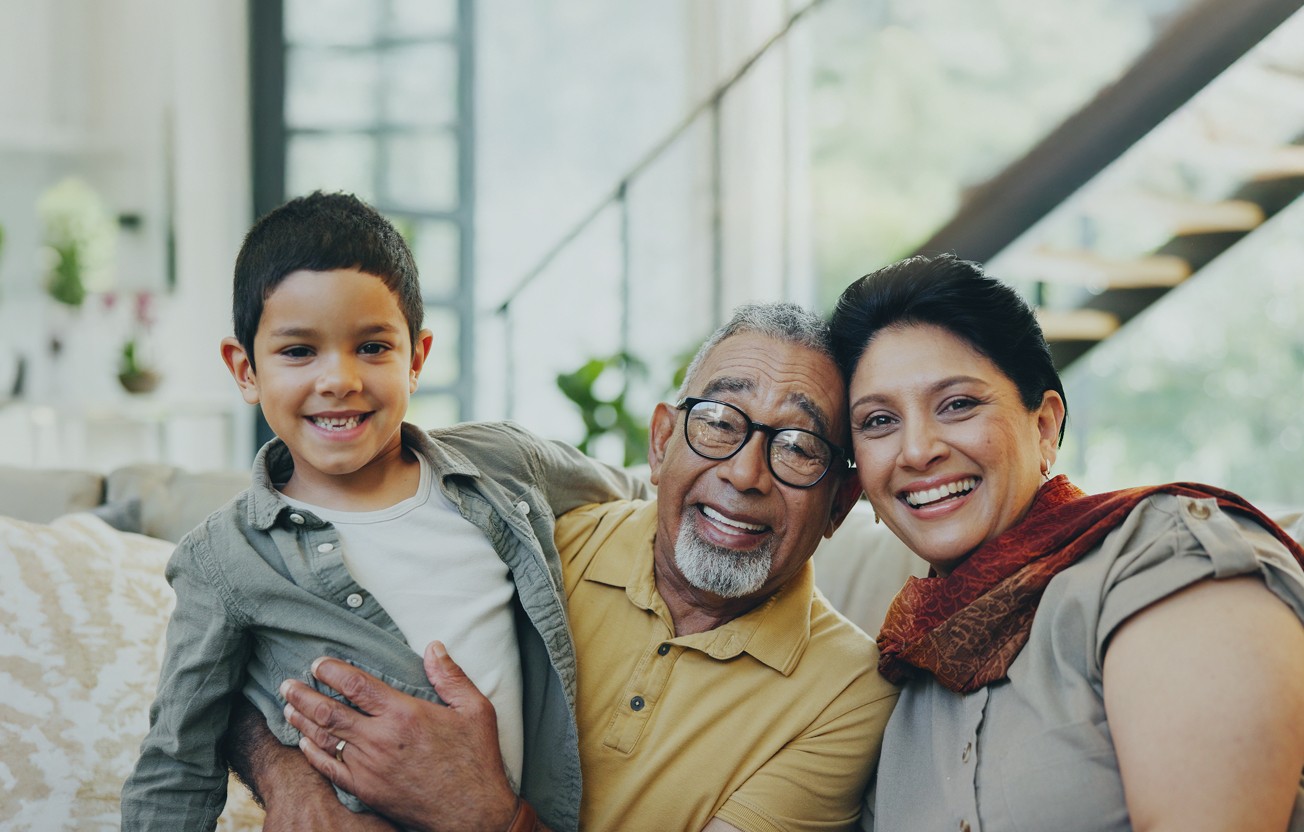A joyful, close-up photo of a smiling young boy with his happy grandfather and grandmother indoors