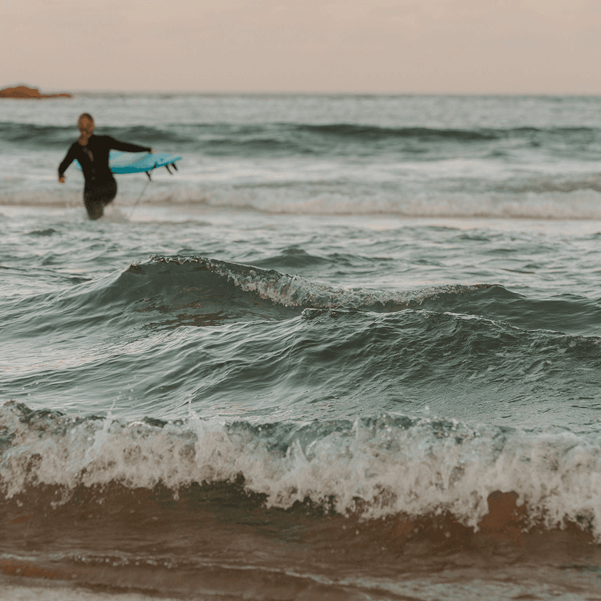 Surfer with blue board wades into the sea.
