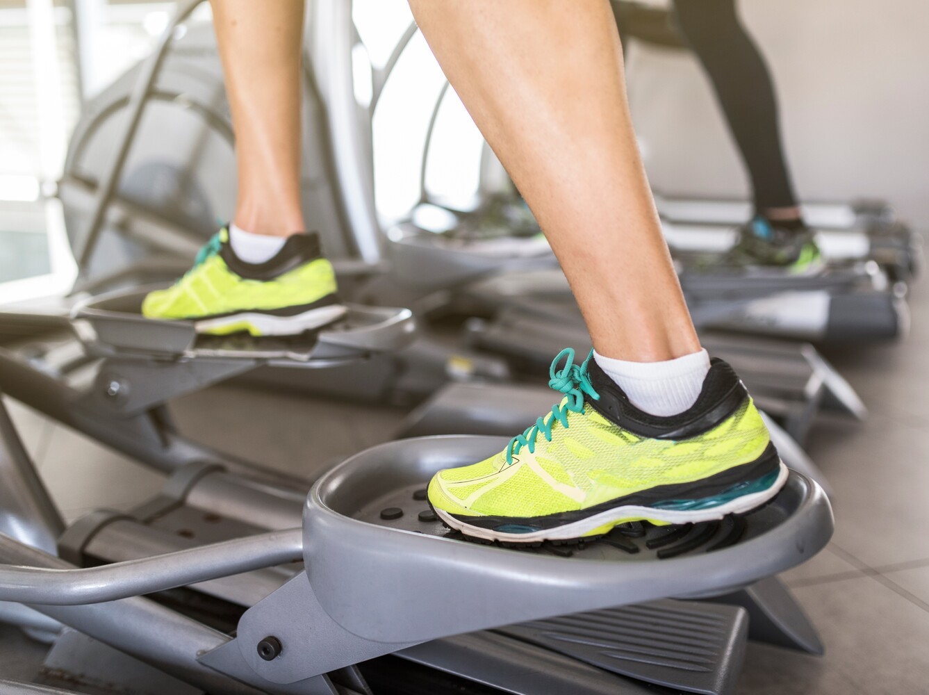 shot of woman’s feet wearing bright sneakers while using an elliptical machine for weight loss in a gym