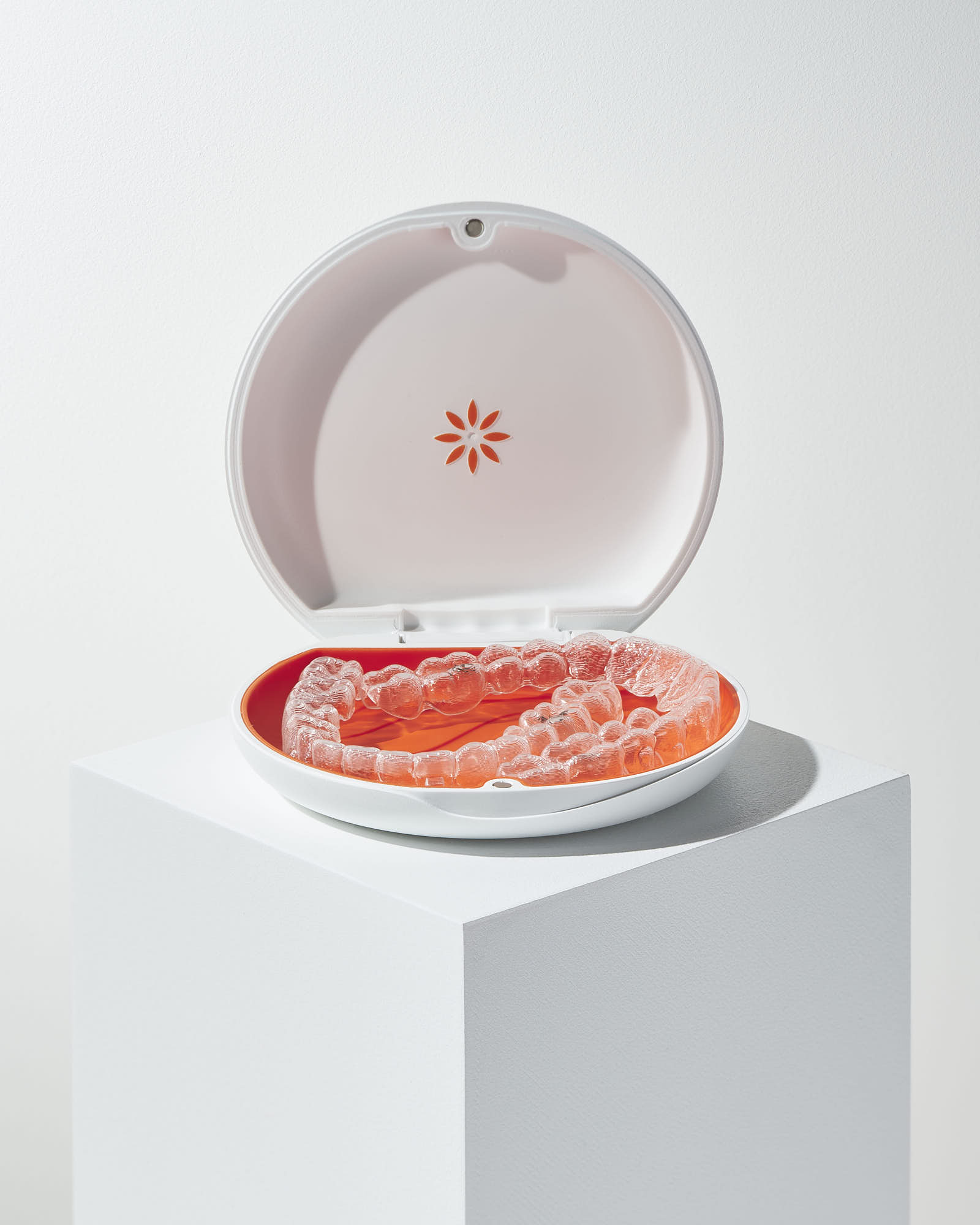 Clear dental aligners in a stylish open case on a white pedestal.