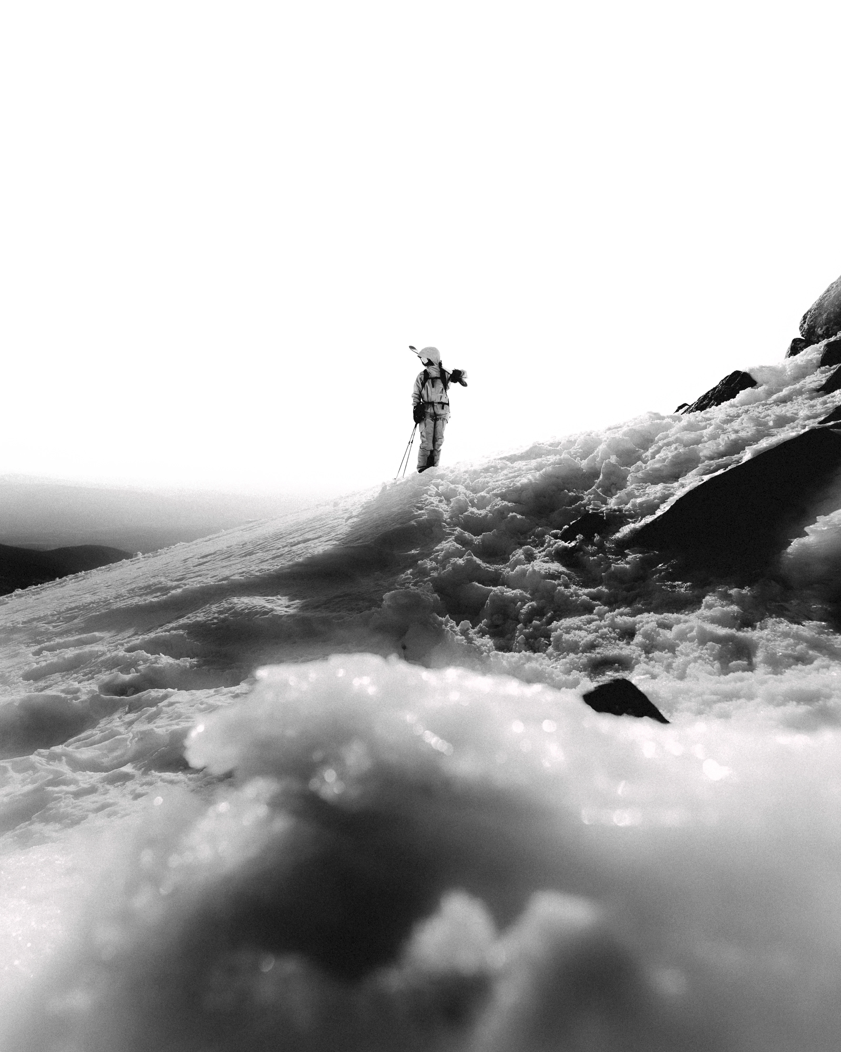 skier walking up a mountain in a black and white picture.