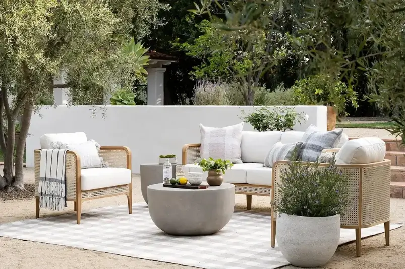 Modern wood and cane outdoor sofa and chairs set with concrete coffee table on a patio rug.