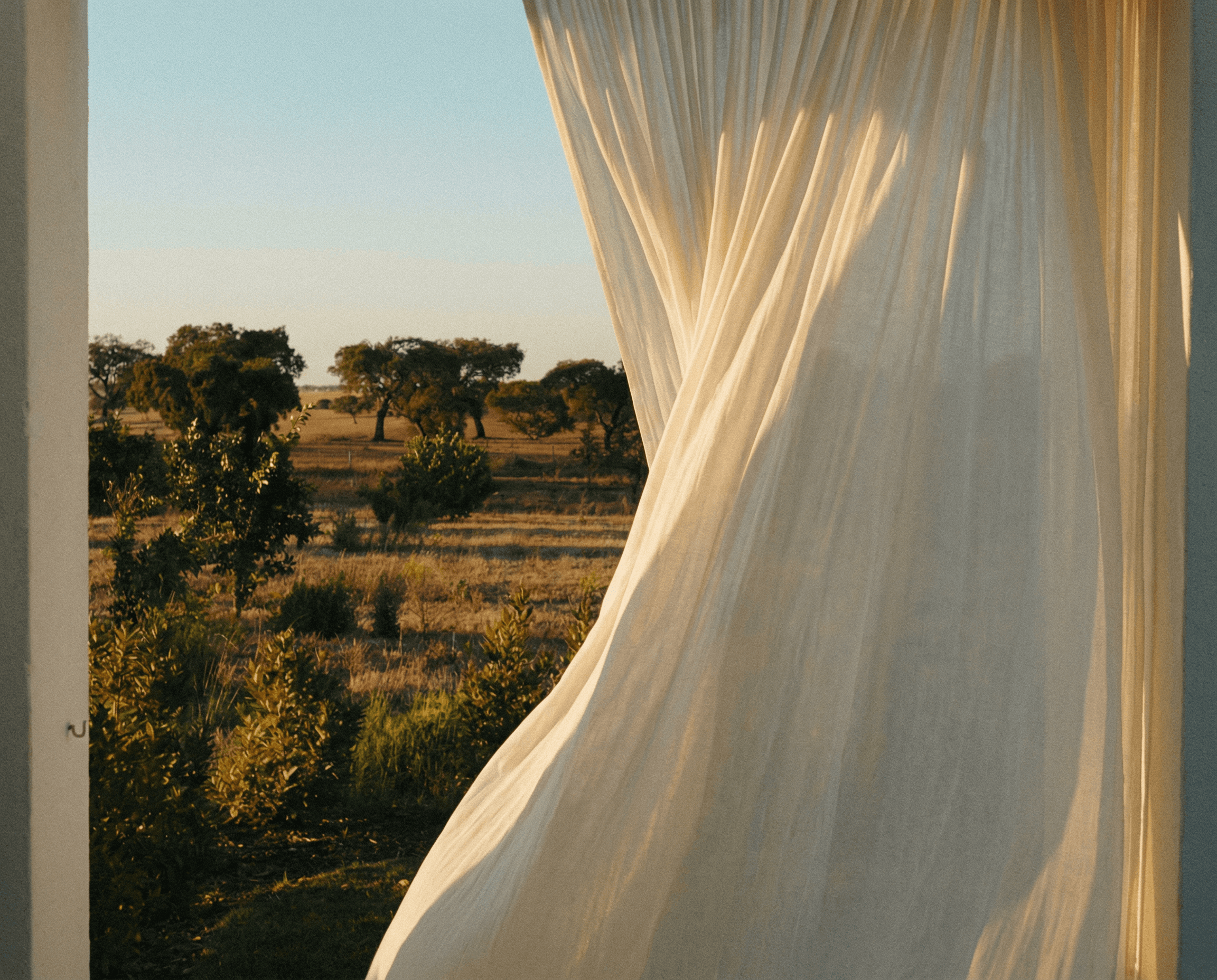 curtains slowly moving in the summer breeze at golden hour, with an Italian countryside in the back