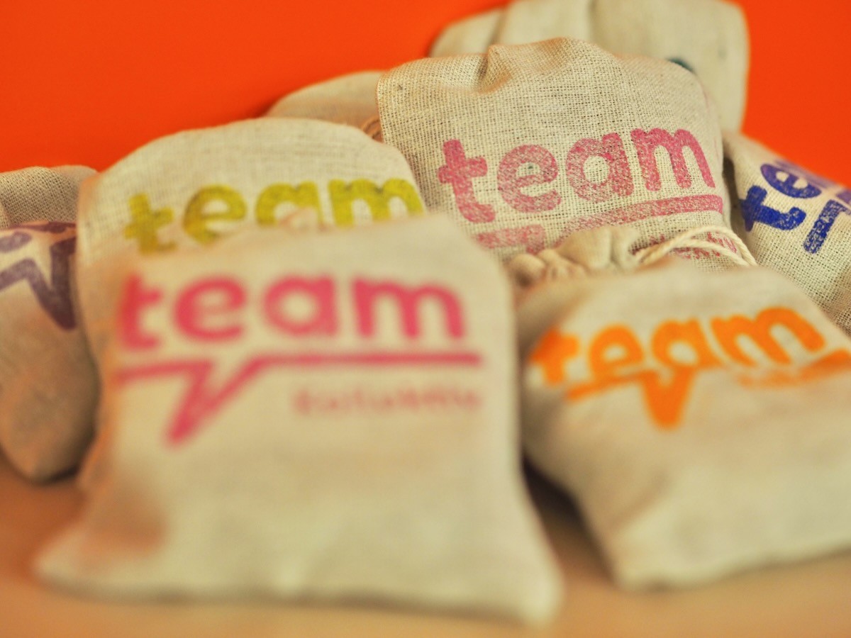 Smiling young woman with long hair standing against a dark green background, holding a finger to her chin.