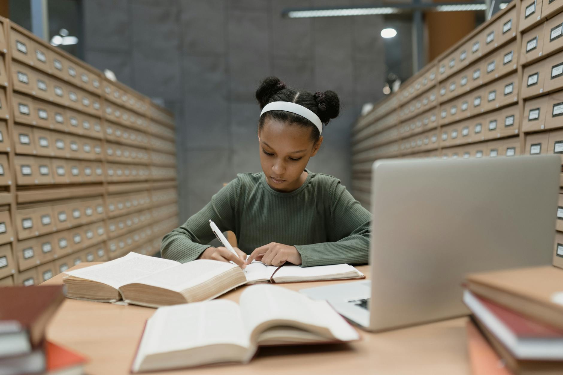 Middle school students sit in a modern library lounge discussing a digital book on their laptops.
