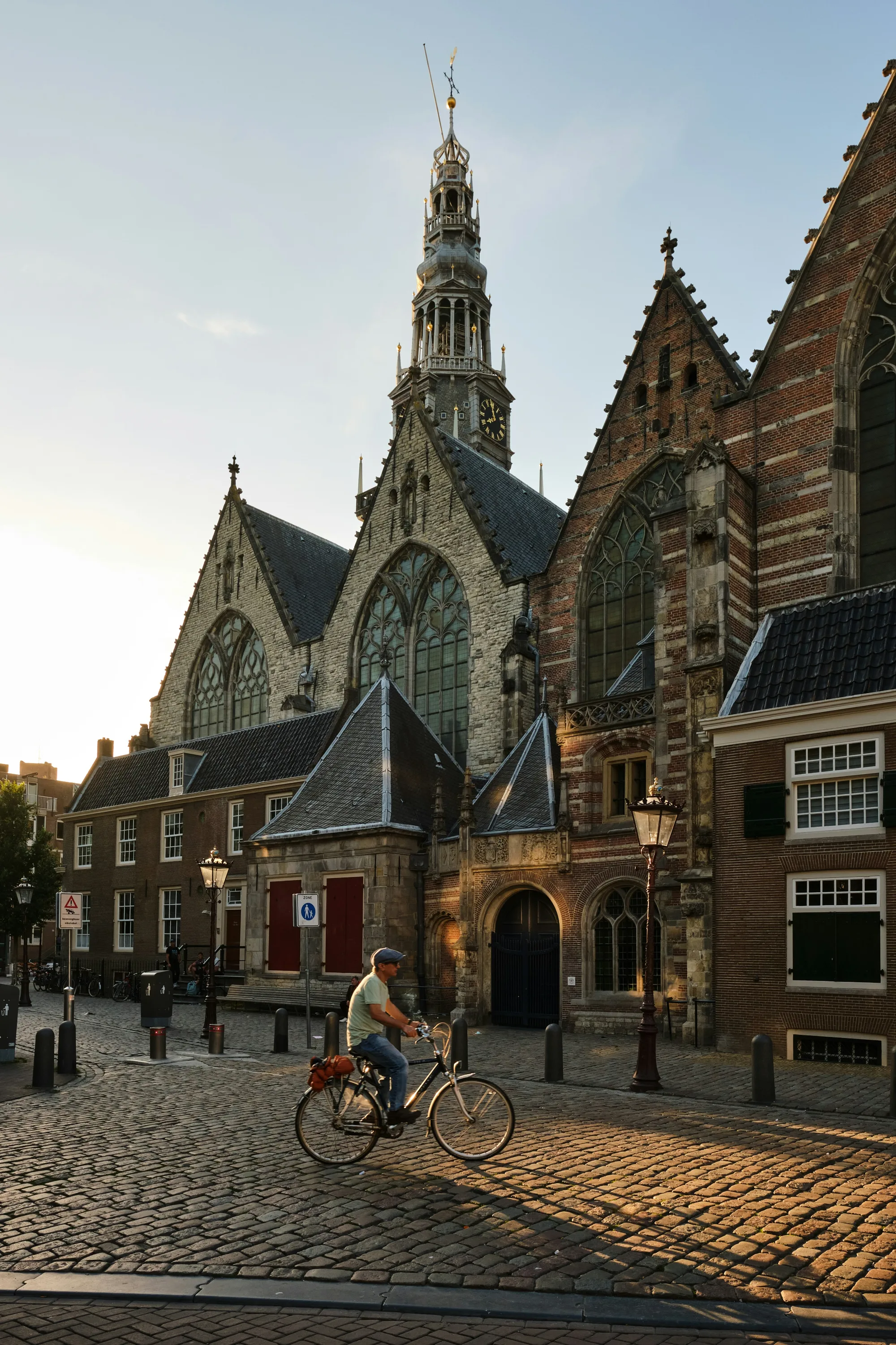 Man cycles past Westerkerk church in Amsterdam during golden hour, cobblestone street
