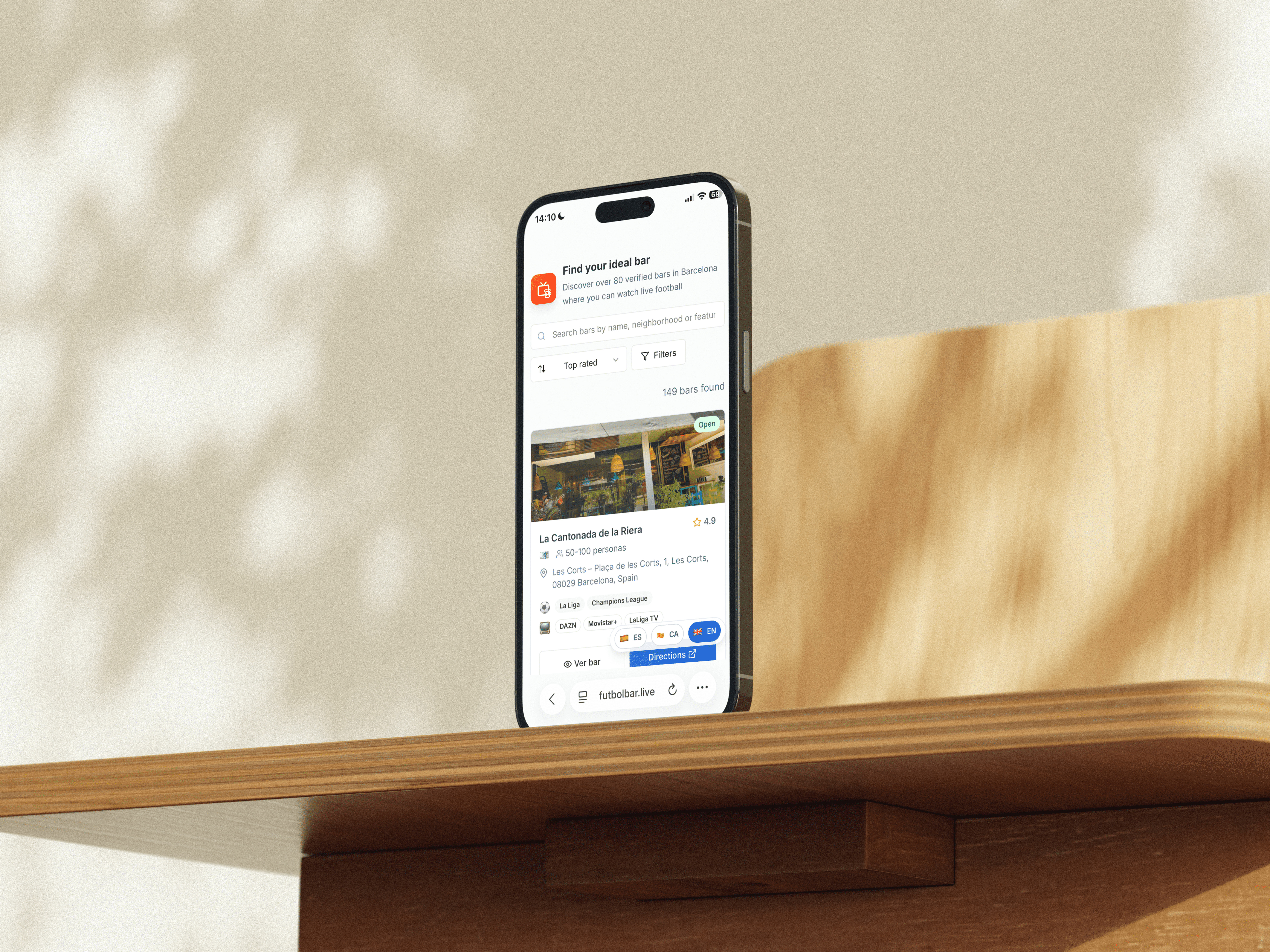 Mobile phone on a wooden surface displaying FutbolBar app bar details and match listings in a clean modern layout