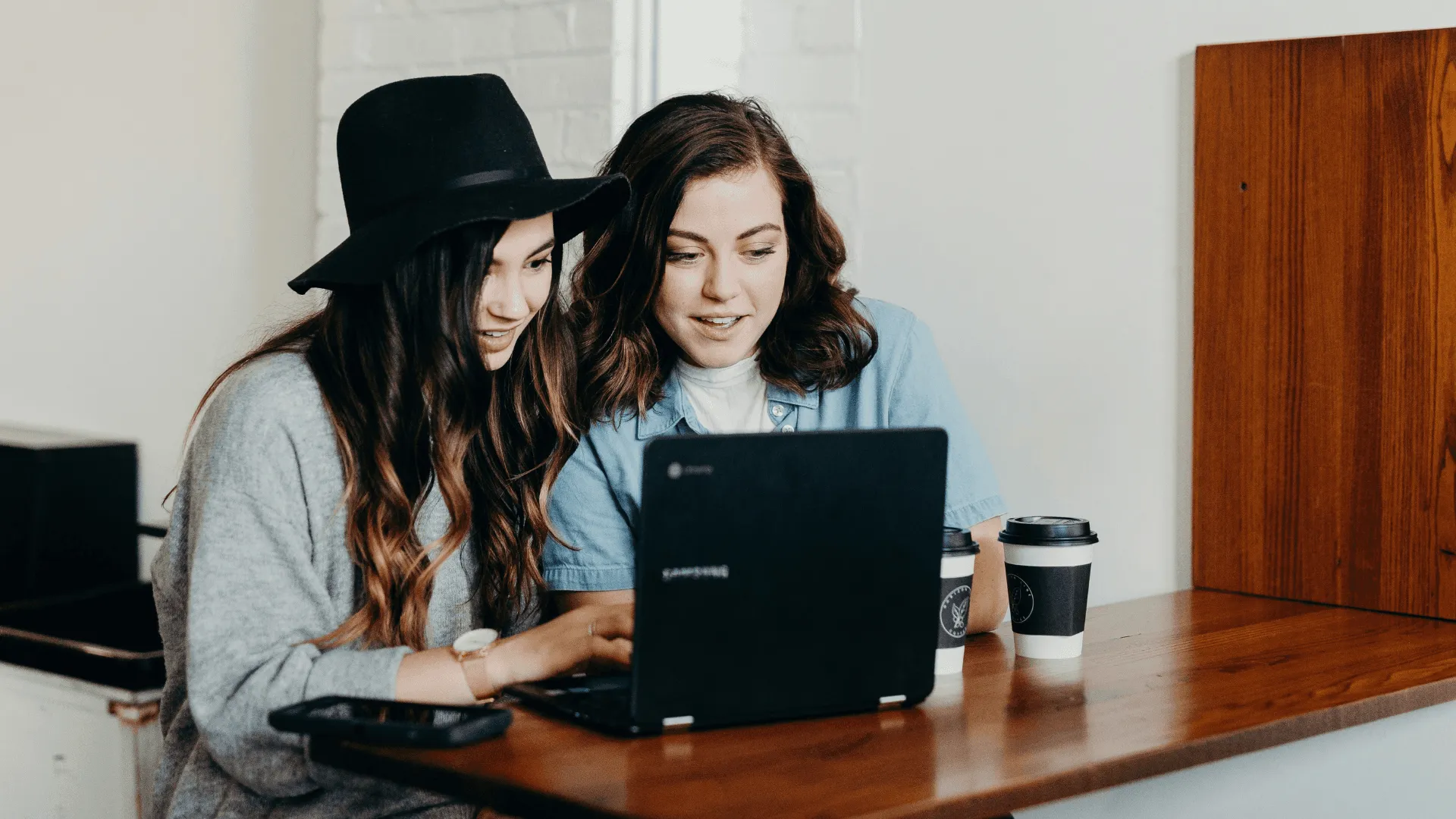 Two girls, sitting together, look at a laptop screen