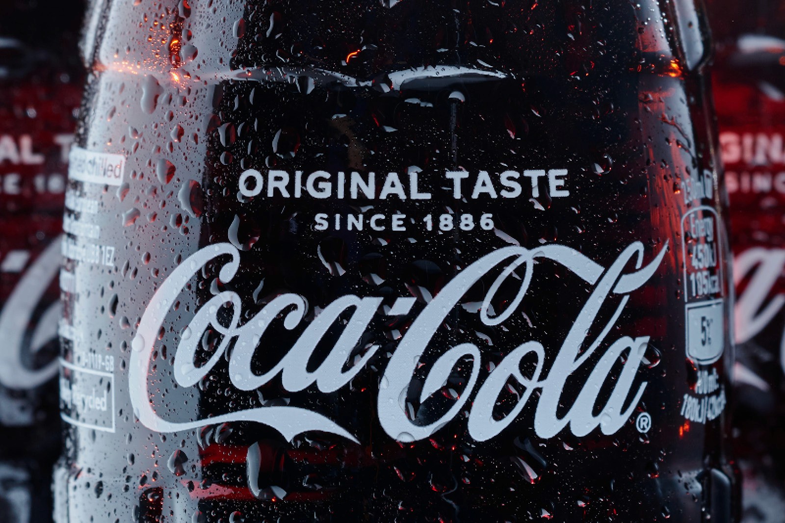 A close-up of a Coca-Cola glass bottle covered in water droplets, showcasing the iconic logo and highlighting the text "Original Taste Since 1886" on the label.
