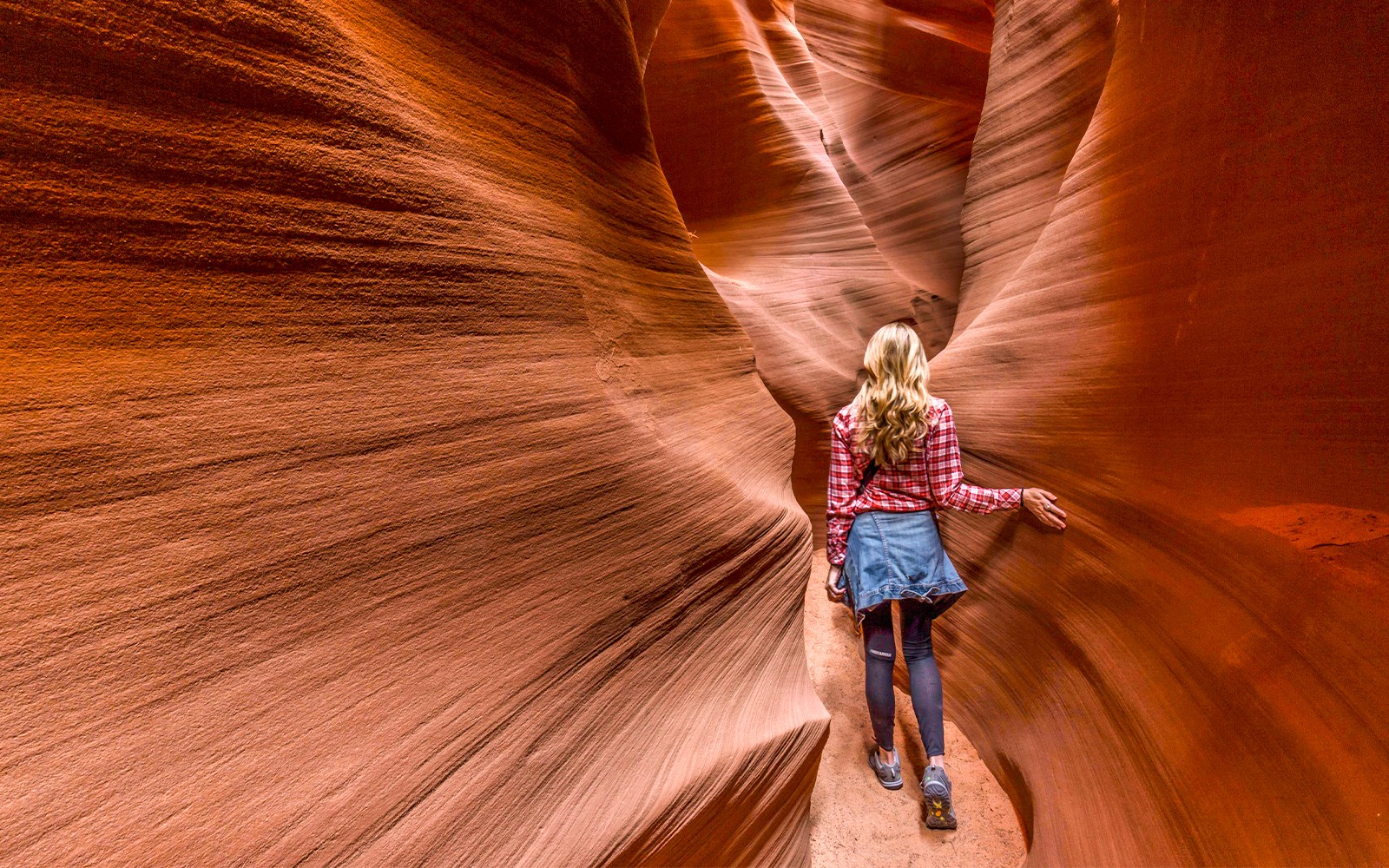 Person walking through narrow sandstone walls in Secret Antelope Canyon.