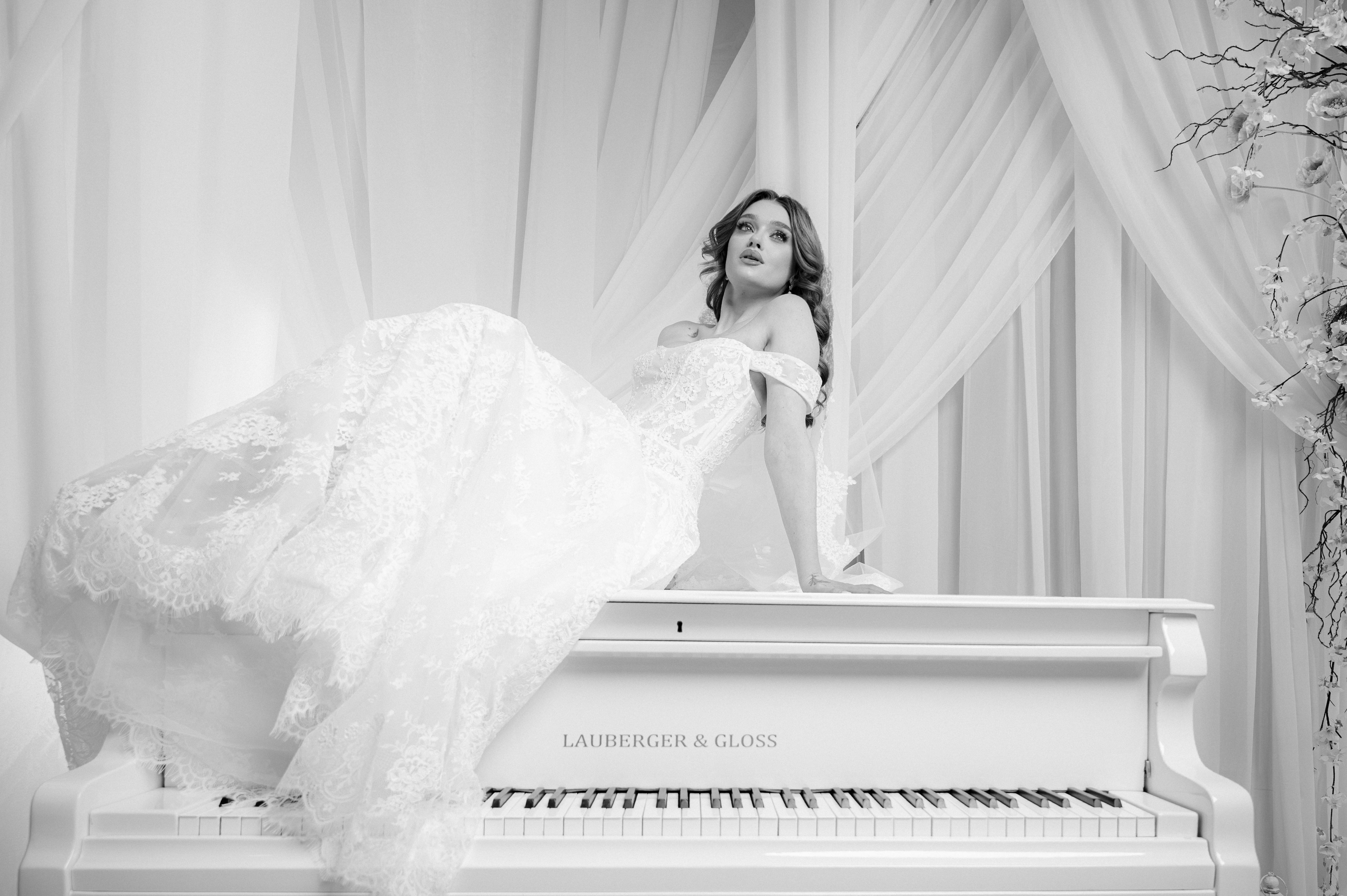 Mireasă fotografiată alb-negru pe un pian alb într-un decor elegant și romantic, fotografie bridal în București