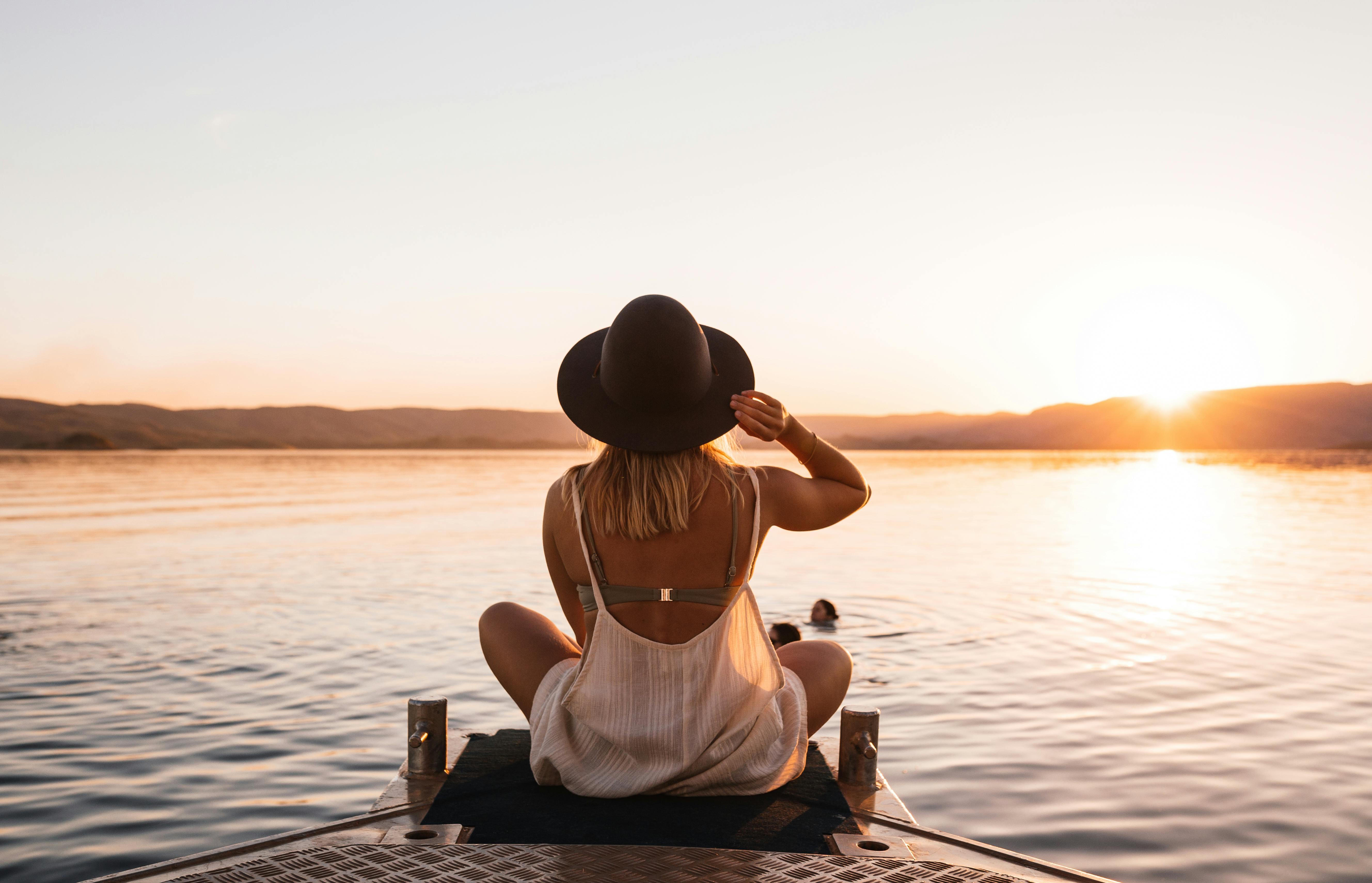 woman in a hat on the lake shore at sunset