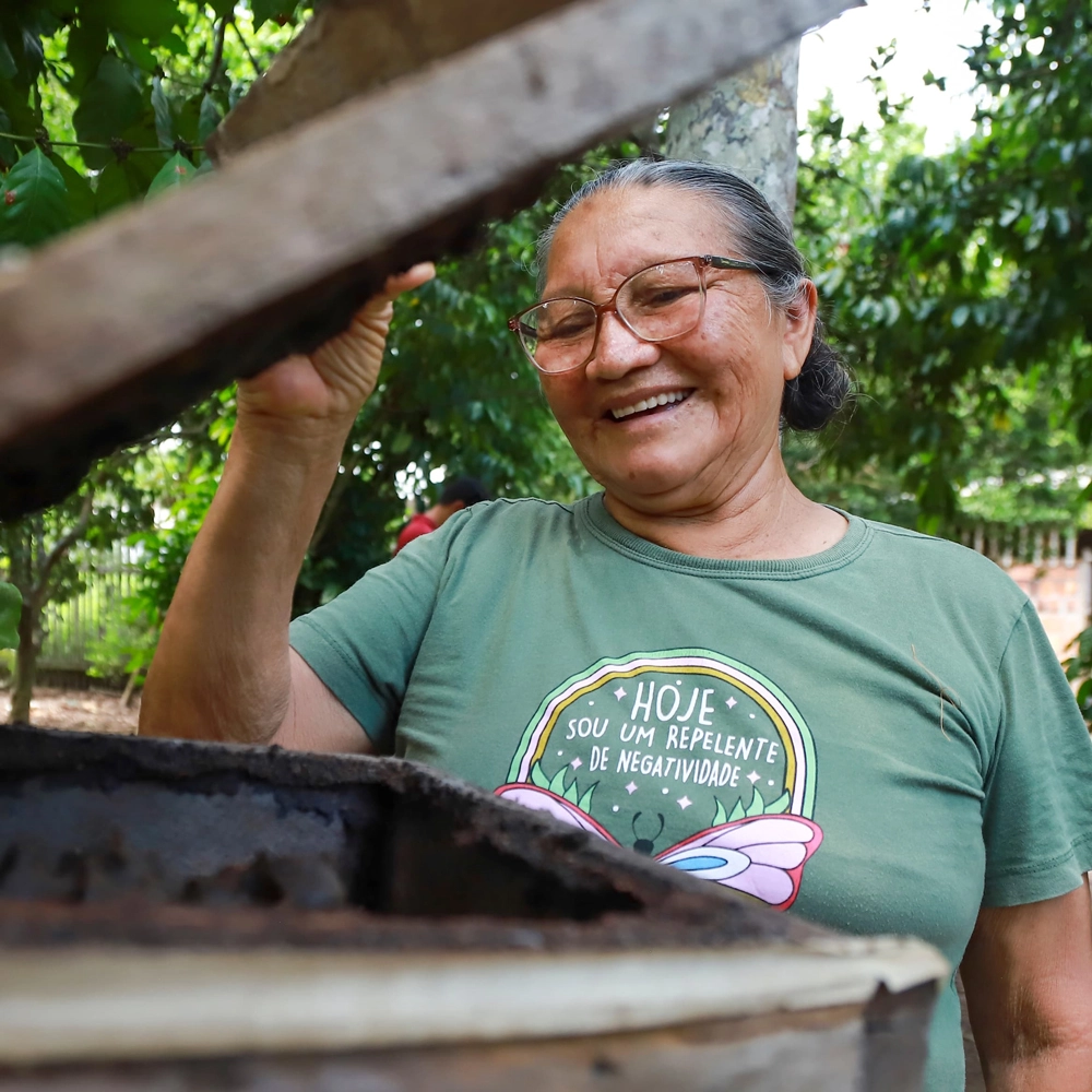 Mulher meliponicultora sorridente abrindo uma melgueira