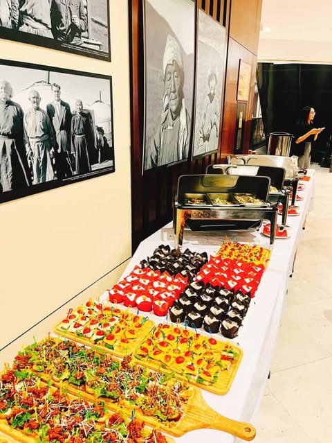 A smiling woman with her arms crossed, standing against a dark green background. She has long, dark hair.