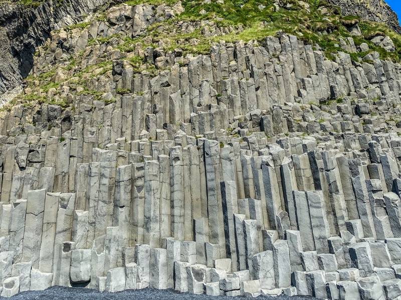 Tall hexagonal basalt columns at Reynisfjara beach in Iceland, formed by cooling lava, creating a geometric wall of vertical stone pillars along the cliff.