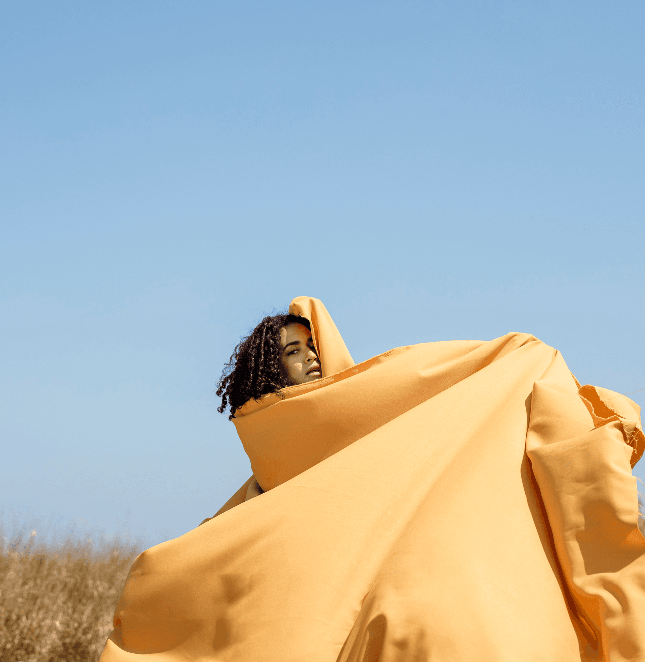 Creative portrait of a woman in yellow flowing fabric outdoors.
