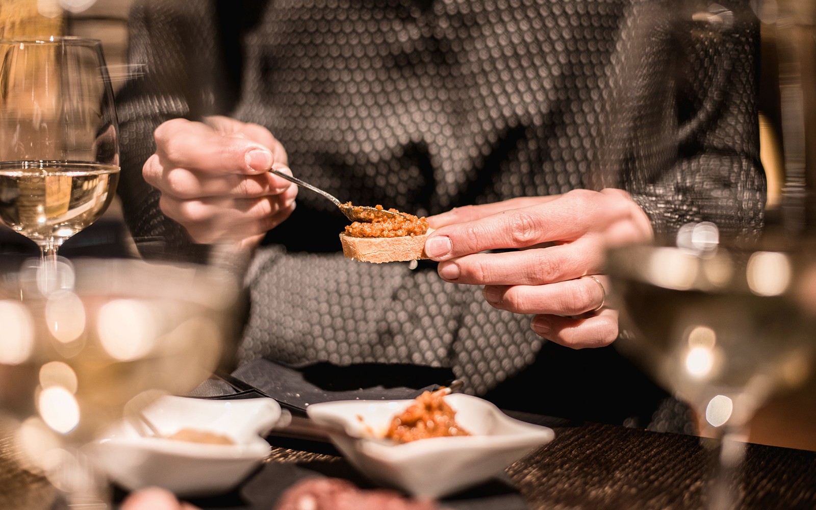 Person, die in einem privaten Weinkeller während einer Weinprobe Tapenade auf Brot streicht.
