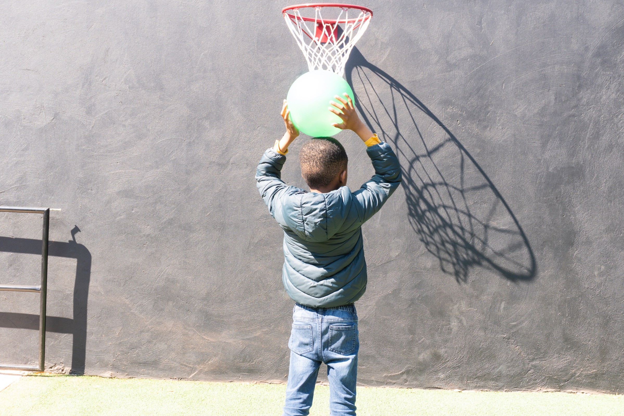 A learner shooting a ball at a basketball hoop outdoors