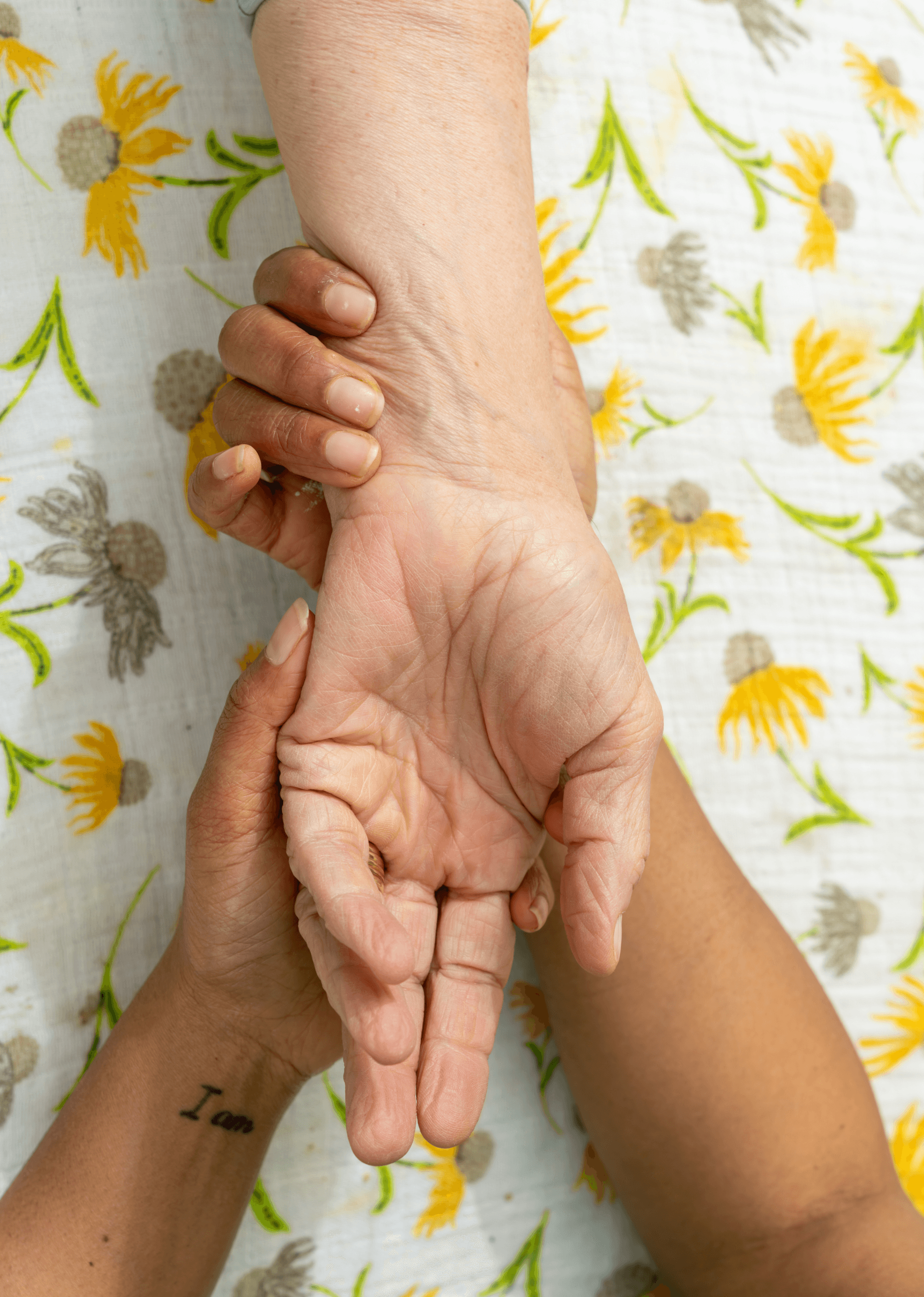 A supportive hand gently holds another on a floral-patterned fabric, symbolizing care and connection, reflecting themes of Louisville postpartum support.