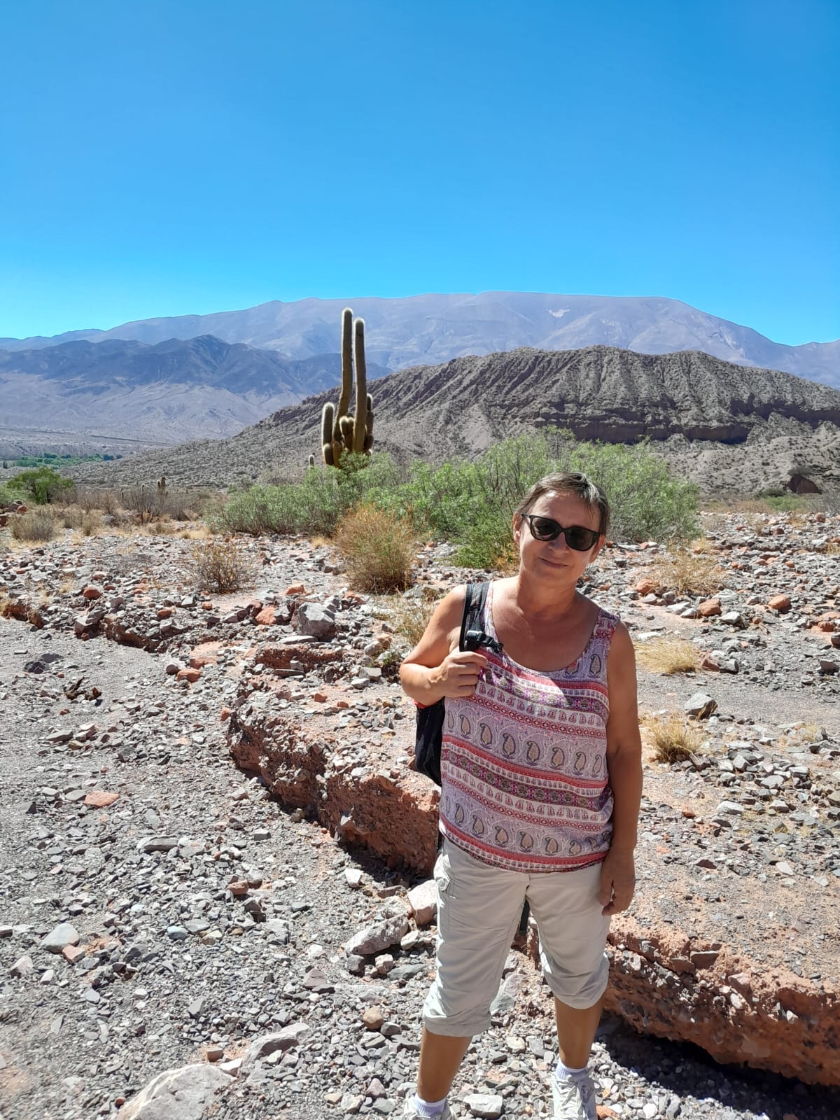 Mujer sentada sobre un tronco frente a una cascada doble en un bosque frondoso de Argentina.
