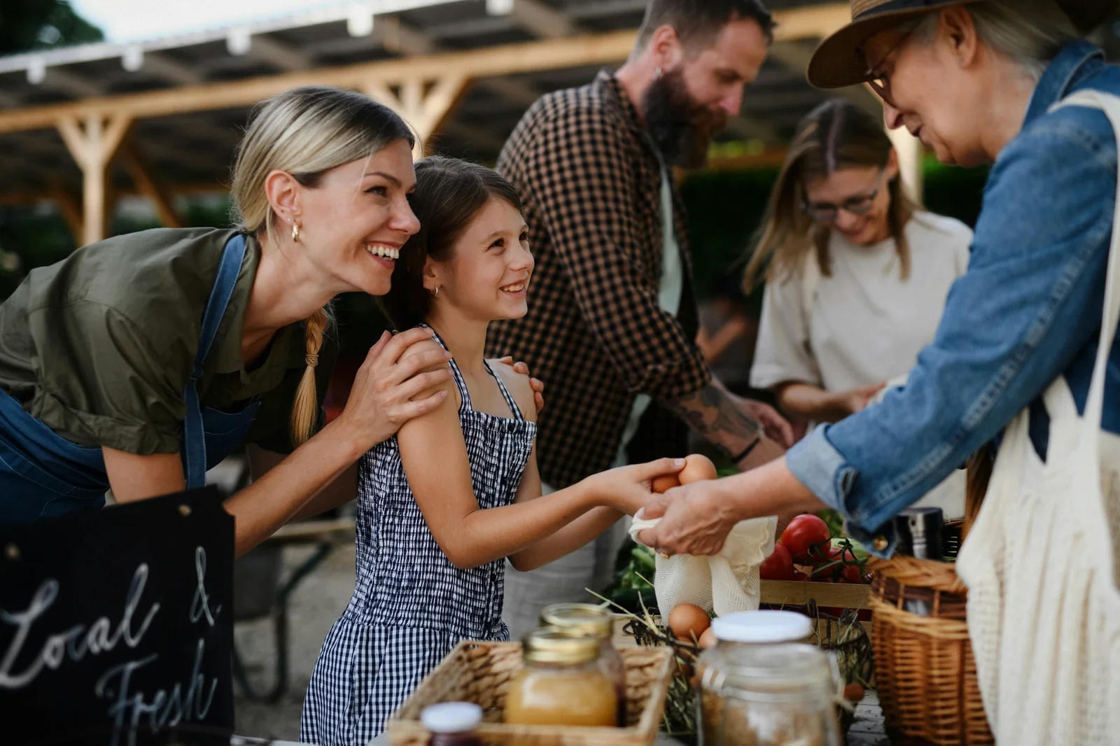 Family and customers at farmers market stand exchanging fresh produce and homemade goods, demonstrating local business engagement.