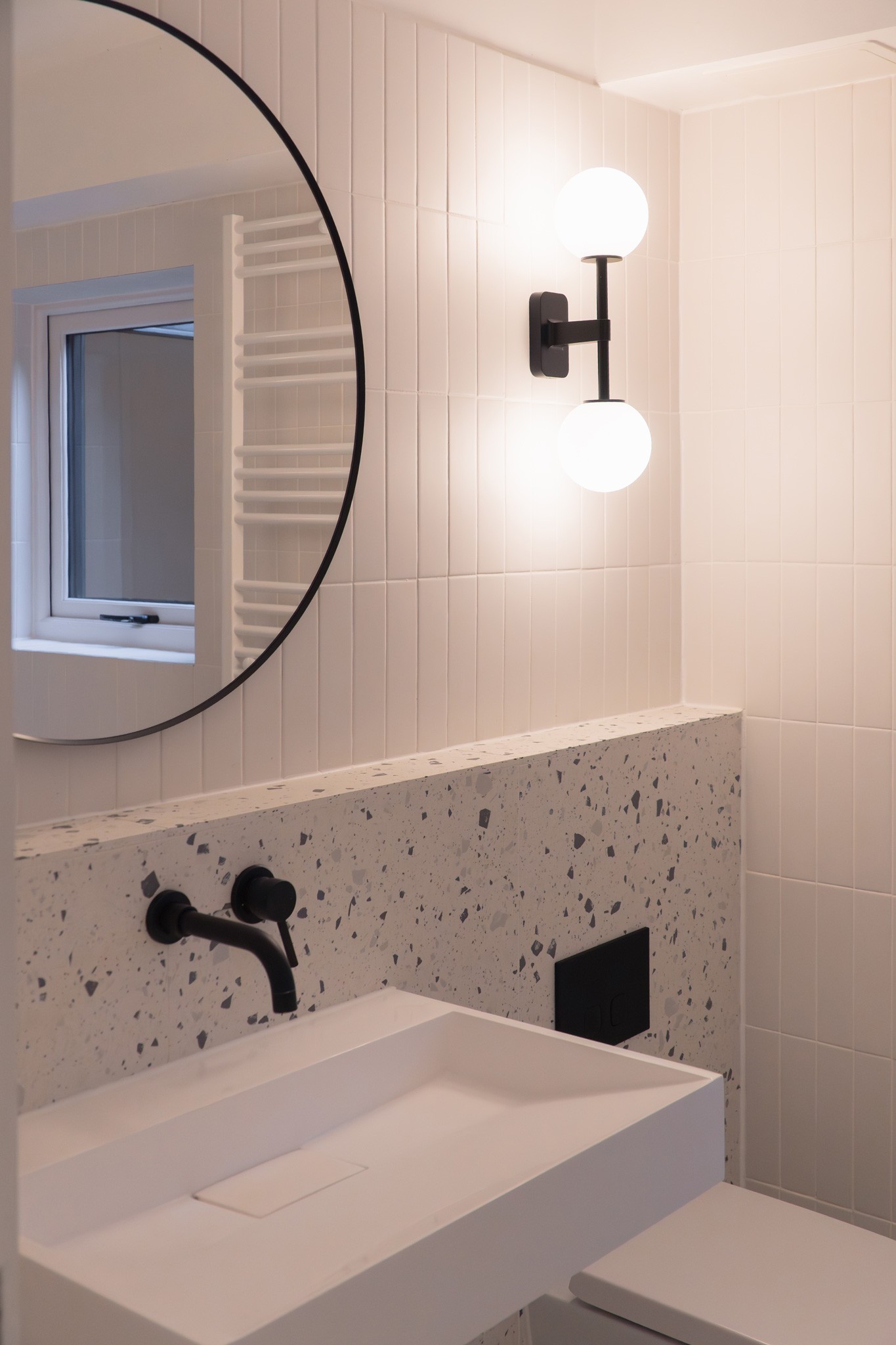 Architect-designed bathroom with terrazzo splashback tiles, white rectangular sink, black wall-mounted taps, round mirror and globe wall light