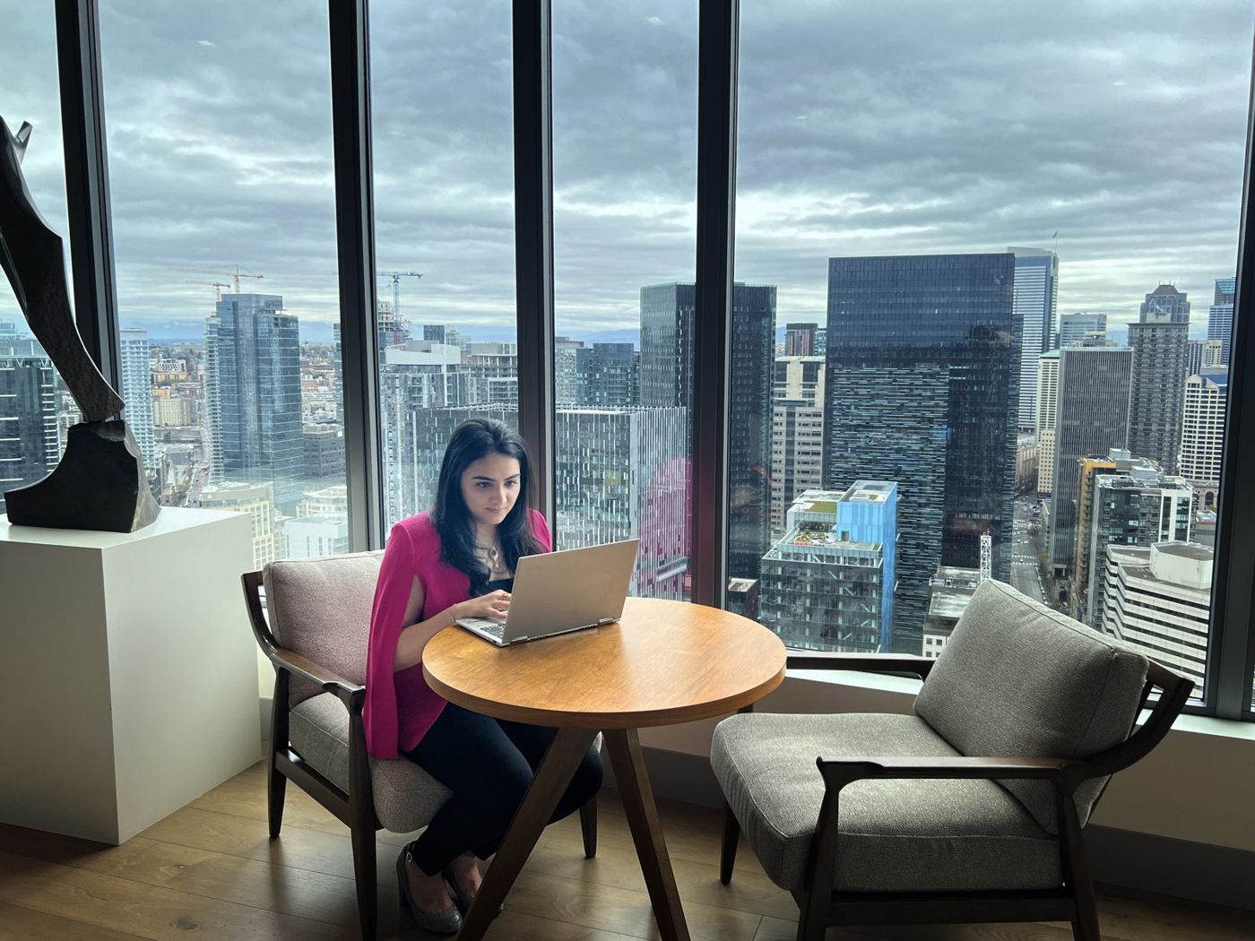 Karishma working on her laptop by floor-to-ceiling windows overlooking the Seattle skyline