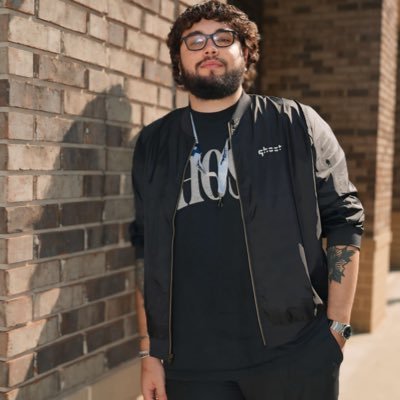 A woman with short curly hair wearing a black t-shirt looks into the camera.