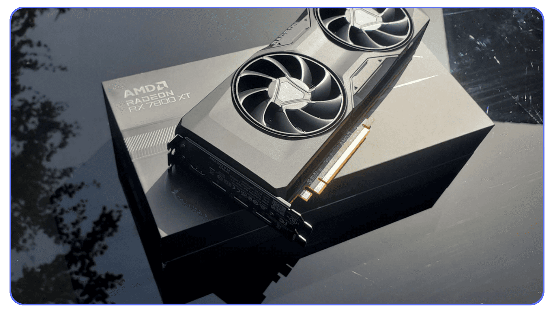 An AMD Radeon RX 7800 XT GPU resting on its box with a reflective black surface underneath.