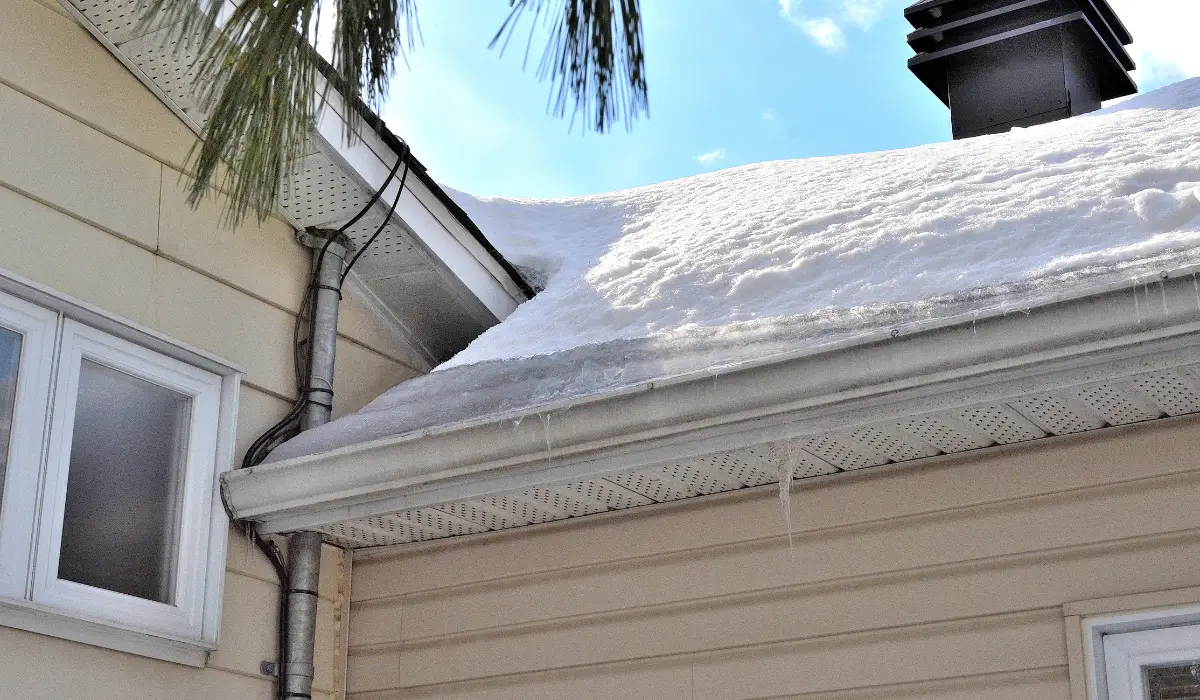 Snow-covered roof with visible ice dam forming due to poor roof ventilation and trapped attic heat