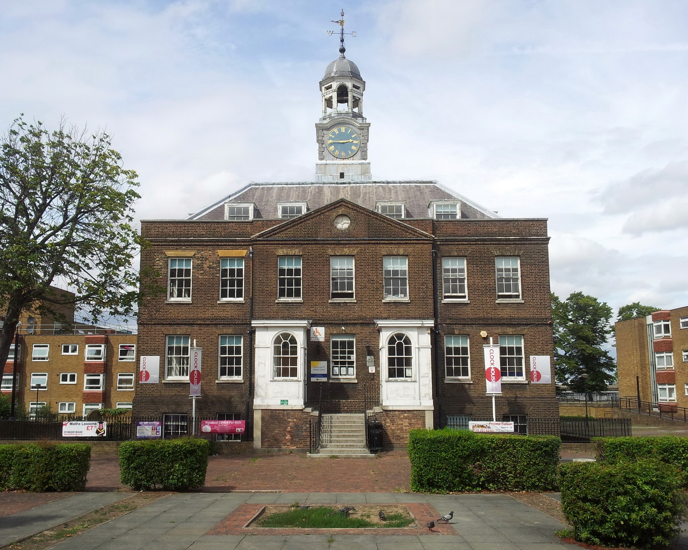 A smiling man with curly hair is sitting at a desk, looking at the camera, with a laptop and a lamp in the background.