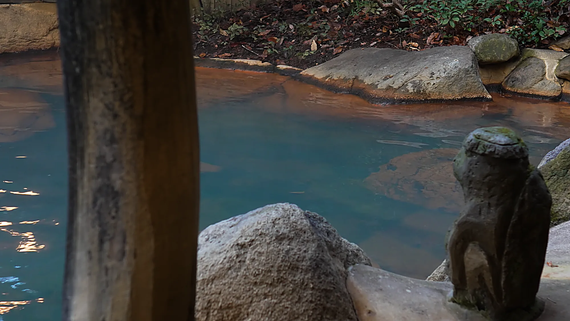 A milky blue hot-spring pool with a stone rim and a small stone figure